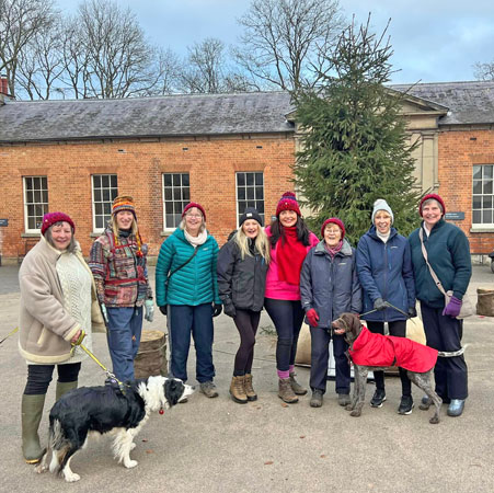 Several ladies and dogs stand in front of a Christmas tree at Attingham