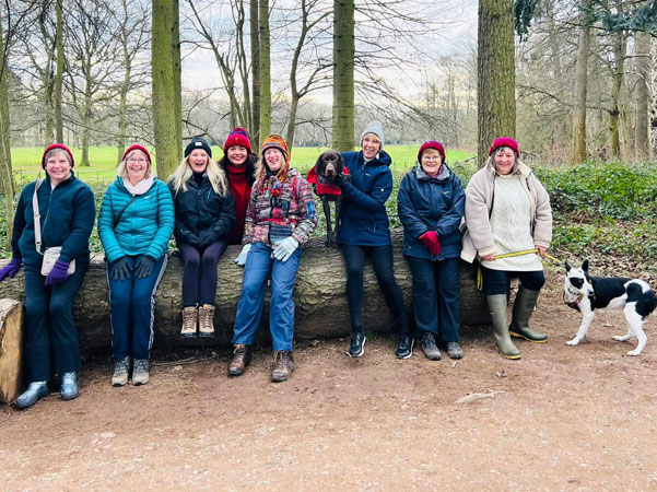 Eight ladies and dogs sit on a fallen tree