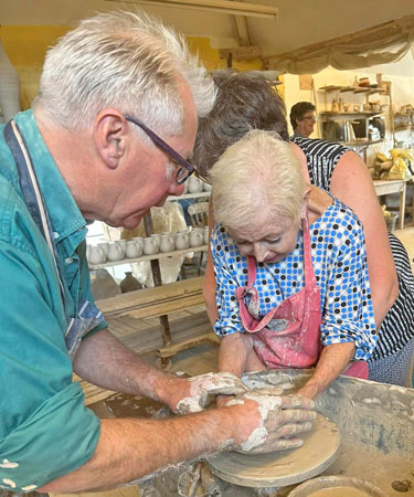 The potter helps one of the ladies create a pot on the wheel