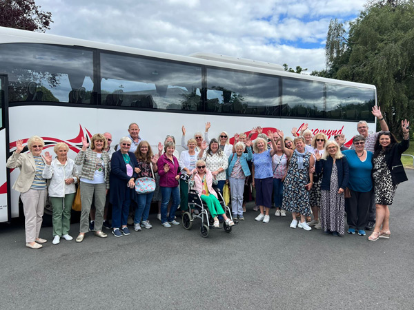 A large group of people stand outside a coach