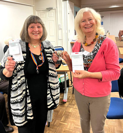 Two ladies hold vouchers and a trophy