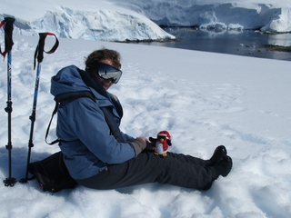 Pen Turner sitting on the snow in the Antarctic. The sea is in the distance.