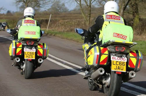 Two Blood Bike riders on their motorbikes, view from behind on a main road.