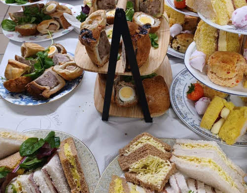 An afternoon tea spread of sandwiches, savouries and cakes on tiered plates. © Severn Hospice Refresh Café