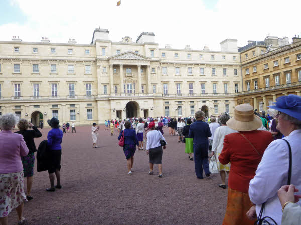 Several WI members in their best outfits walking across the parade ground at Buckingham Palace, which can be seen at the rear of the picture.
